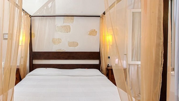 Habitación de hotel estrecha con una cama individual, cabecero de madera y pared con diseño geométrico.