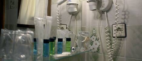 A bathroom with two hair dryers mounted on the wall, a glass shelf with toiletries, and a floral-patterned tile backsplash.