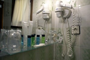 Un baño con dos secadores de pelo sujetos a la pared, un estante de vidrio con artículos de aseo y un salpicadero de azulejos con estampado floral.