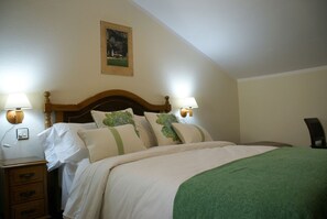 Una cama bien hecha con cabecera de madera, dos lámparas de noche, una mesita de noche con cajones y un cuadro enmarcado en la pared.