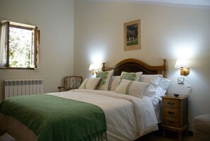 Un dormitorio con cama, lámparas de noche, un radiador, una ventana y un cuadro en la pared.