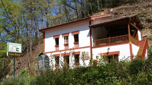 A rural house with a balcony, surrounded by trees and vegetation. - Casa Rural Priena (Cangas de Onis)