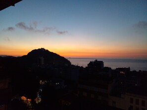 A coastal cityscape at dusk with a prominent hill and buildings in the foreground. - Babilonia Rio Hostel (Rio de Janeiro)