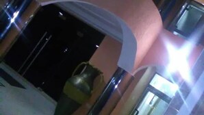 A corridor with a curved wall, a metal trash bin, and a glass door leading to a room. - Jewima Hotel (Accra)