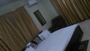 A hotel room with a bed, curtains, a small table, and a wall-mounted air conditioner. - Jewima Hotel (Accra)