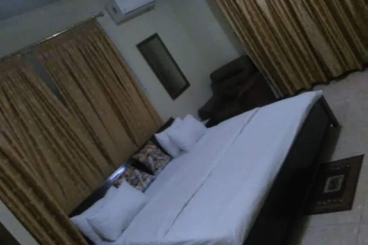 A hotel room with a bed, curtains, a small table, and a wall-mounted air conditioner.