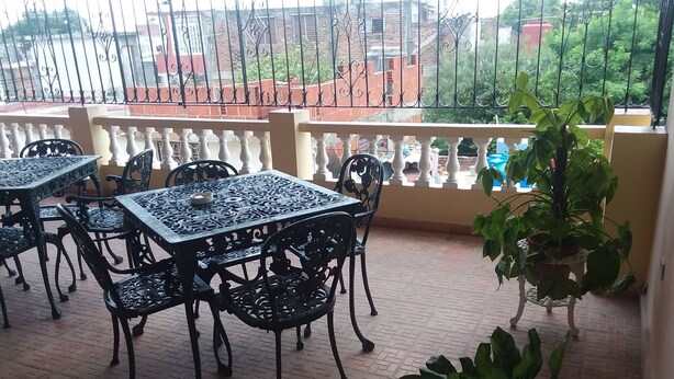 A balcony with a tiled floor, metal tables and chairs, and a potted plant. - Hostal En Casa (Bayamo)