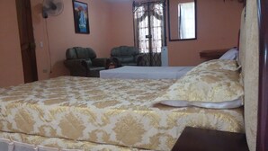 A bedroom with a large bed, two chairs, a fan, a window with curtains, and a mirror. - Hostal En Casa (Bayamo)