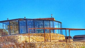 A stone building with a glass enclosure, featuring a metal railing and a flag on top. - Edom camp (Dana)