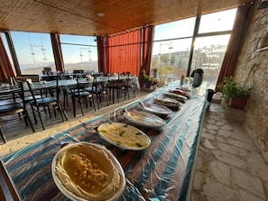 A dining area with a long table covered with food, surrounded by chairs, and large windows offering a view.