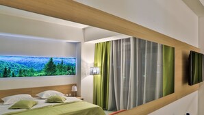 Une chambre d’hôtel moderne avec un grand lit, un téléviseur fixé au mur et une fenêtre donnant sur une forêt.