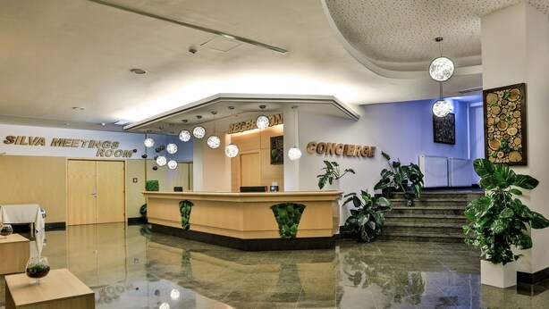 Un hall d’hôtel comprenant un comptoir d’accueil, une « salle de réunion Silva » et un panneau indiquant le « service de conciergerie ».