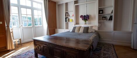 Een slaapkamer met een groot houten bed, inbouwkasten en een uitzicht op het exterieur door een groot raam.