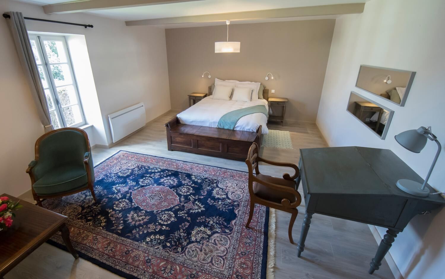 Een slaapkamer met een bed, een bureau, een stoel, een vloerkleed en een raam.