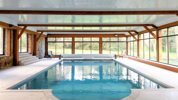 Una piscina interior con paredes de piedra, vigas de madera y amplios ventanales que ofrecen vistas al exterior.