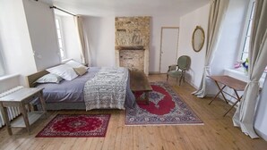 Un dormitorio con cama, chimenea de piedra, una mesita y una ventana con cortinas.