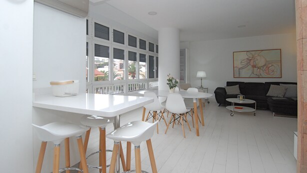 A modern living room with a dining area, white furniture, and large windows.