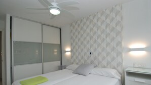 A hotel room with a bed, a ceiling fan, a nightstand, and a wall with geometric patterned wallpaper.