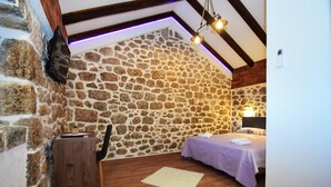 A cozy room with a stone wall, wooden floor, a bed with a purple bedspread, a small wooden table, and a chair. - Holiday Home Ante is set in Starigrad Paklenica. (Starigrad Paklenica)