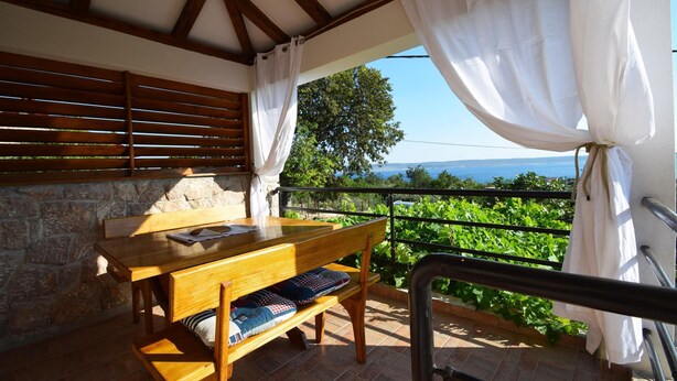 A wooden table with benches, a stone wall, and a view of greenery and the sea. - Holiday Home Ante is set in Starigrad Paklenica. (Starigrad Paklenica)