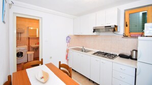 A compact kitchen with white cabinets, a gas stove, a sink, and a washing machine in the adjacent room. - Holiday Home Ante is set in Starigrad Paklenica. (Starigrad Paklenica)