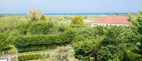 A residential area with a house featuring a red roof, surrounded by lush greenery and a clear view of the sea.