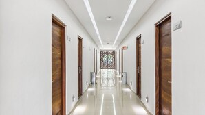 Um corredor longo e bem iluminado, com portas de madeira, placas de número de quarto e um painel de vidro decorativo no final.