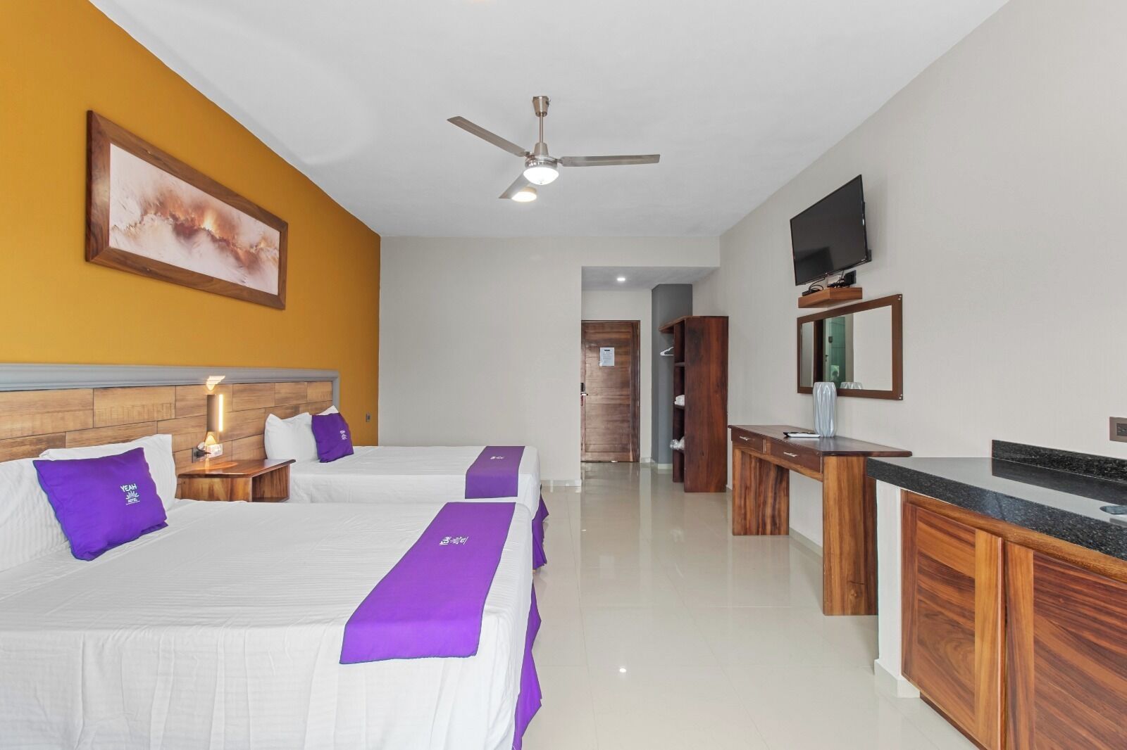 A hotel room with two beds, a desk, a television, and a ceiling fan.
