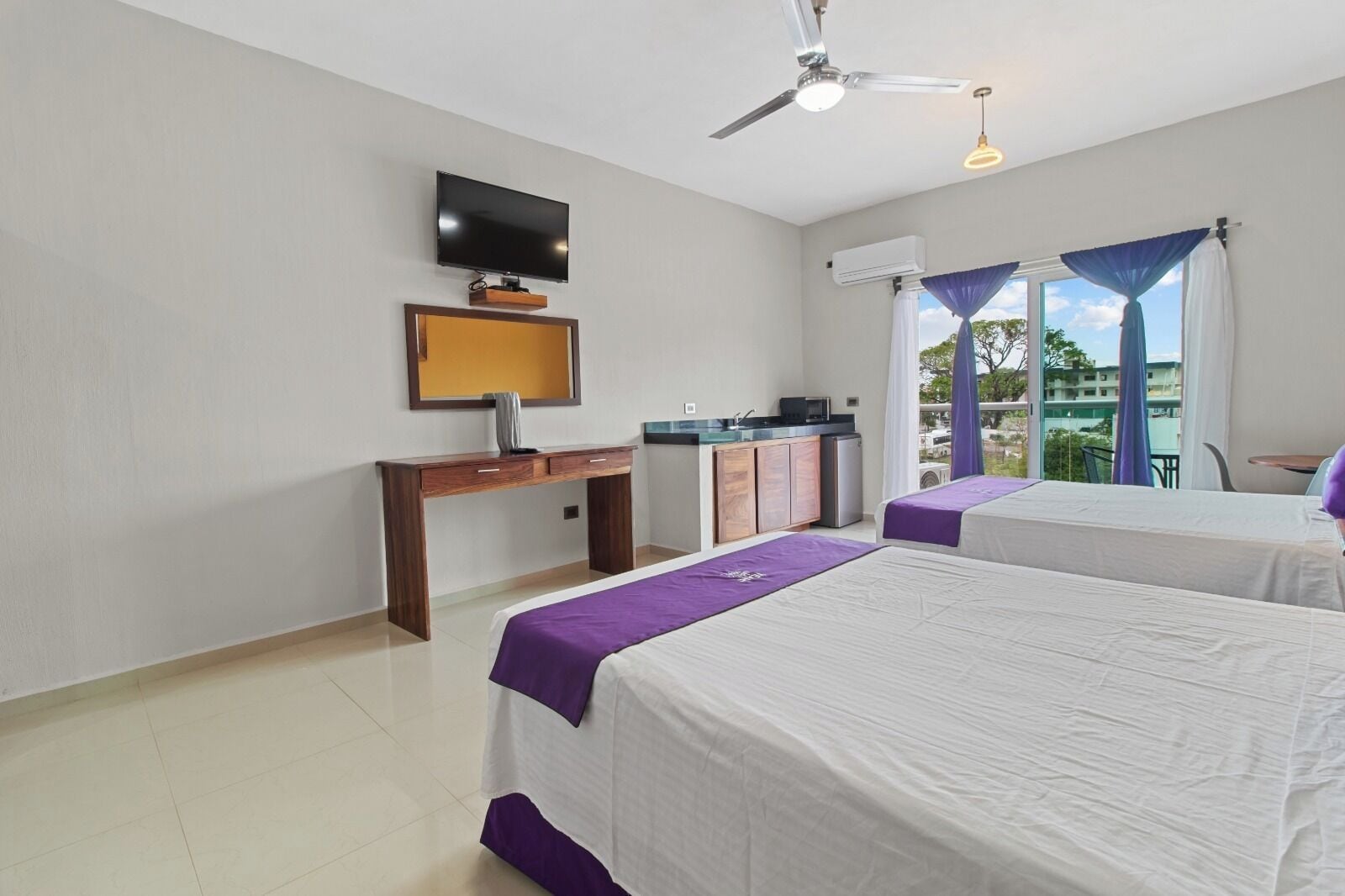 Une chambre d’hôtel avec deux lits, une télévision, un bureau, une kitchenette et un balcon avec vue.