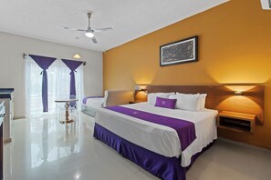 Una habitación de hotel con una cama grande, dos mesitas de noche, un ventilador de techo y una ventana con cortinas.