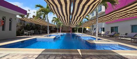 Ein Swimmingpool mit gestreiften Sonnenschirmen, Liegestühlen und Palmen.
