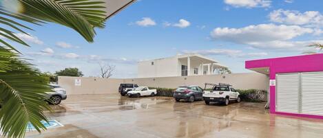 A parking area with several vehicles, a building with a white facade, and a pink structure.