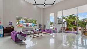 Um lobby de hotel moderno com área de estar, balcão de recepção e grandes janelas com vista para o exterior.