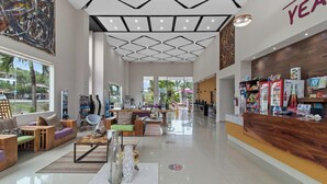 Um lobby espaçoso com design moderno, com uma mesa de recepção, áreas de estar e uma grande janela com vista para o exterior.