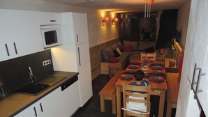 Een compacte keuken met witte kastjes, een ingebouwde magnetron en een vaatwasser. Een eethoek met een houten tafel, gedekt voor vier personen en omringd door stoelen, is zichtbaar.