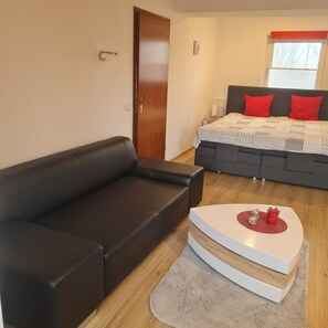Um quarto moderno com um sofá de couro preto, uma cama com almofadas vermelhas e uma mesa de cabeceira com uma luminária.