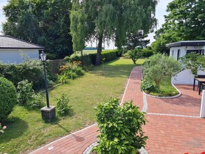 Um jardim bem cuidado com um caminho de tijolos, arbustos variados e um gramado.