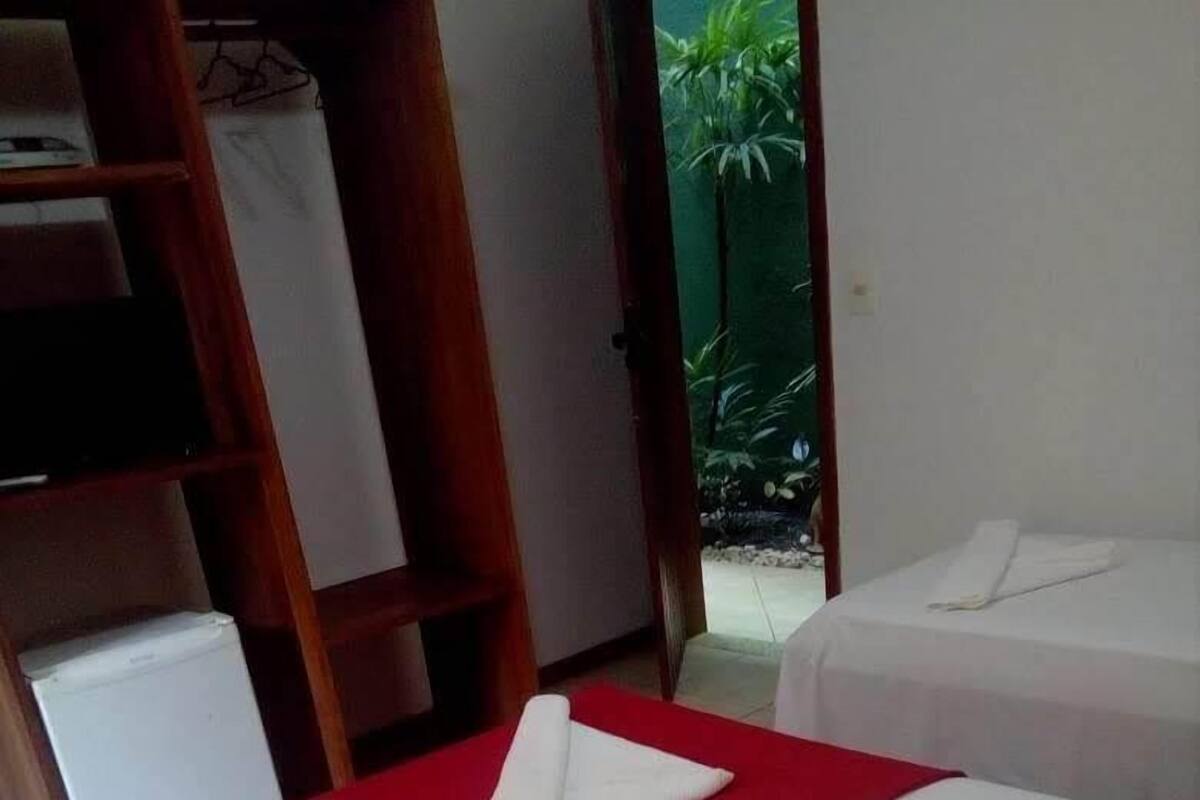 Hotellihuoneessa on kaksi sänkyä, joissa on punaiset päiväpeitteet ja valkoiset lakanat. Huoneessa on myös puinen vaatekaappi ja pieni valkoinen jääkaappi.