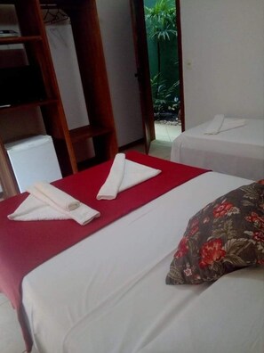 A hotel room with two beds, each with a red bedspread and white linens. There is a wooden wardrobe and a small table with a red tablecloth. - Pousada Uluwatu (Itacaré)