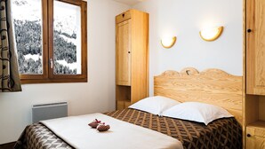 Een slaapkamer met een bed, een raam met uitzicht op een besneeerd landschap, een houten garderobe en een wandlamp.