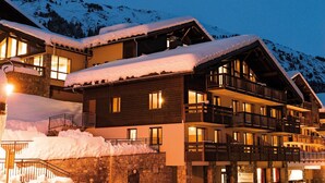 Een meerhoog hotel met balkons en een gevel van steen, omringd door met sneeuw bedekte bergen.