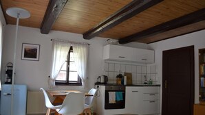 Una cocina compacta con armarios blancos, un horno pequeño y una zona de comedor con mesa y sillas.