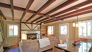 A cozy living room with a fireplace, a sofa, a dining table with chairs, and a staircase.