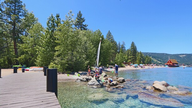 A wooden pier extending into a clear lake with people engaging in water activities.