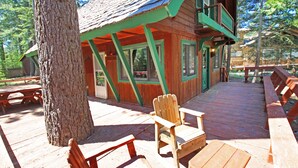 A wooden cabin with a deck, benches, and a chair.