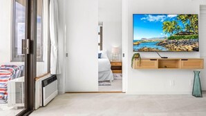 A modern hotel room with a sliding glass door leading to a balcony, a flat-screen TV mounted on the wall, and a wooden console table with storage.
