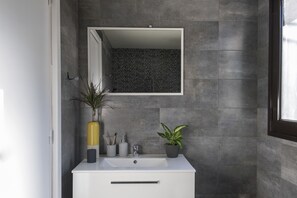Un baño moderno con un lavamanos blanco, un espejo y dos plantas en macetas.