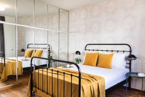 Un dormitorio con cama, mesitas de noche, un espejo y un papel tapiz estampado.