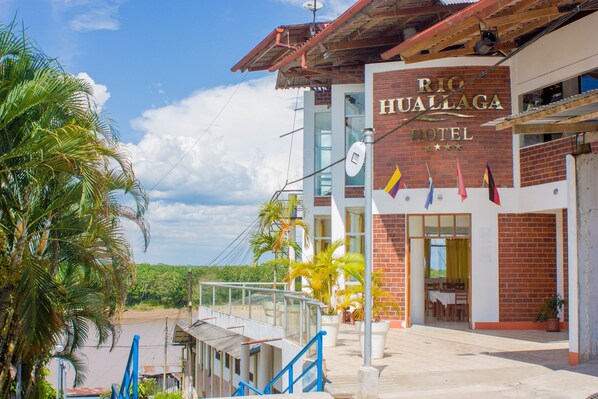 A hotel with a name sign, outdoor seating, and palm trees.