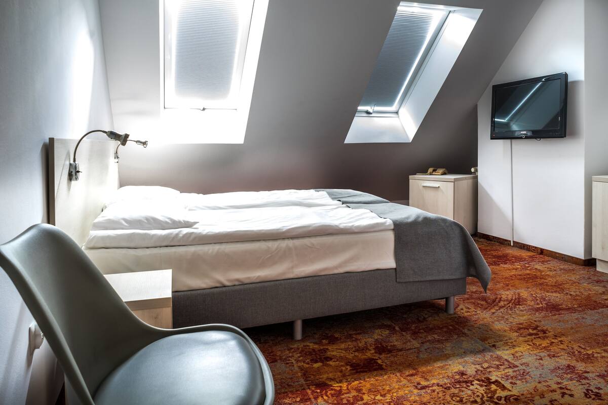 A modern bedroom with a bed, a desk, a chair, a TV, and skylights.